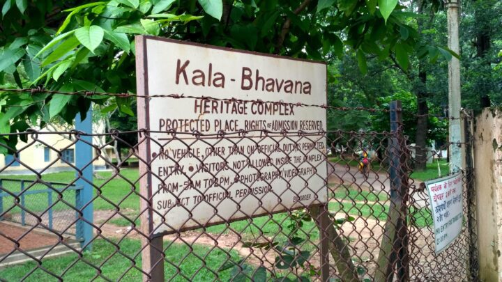 A sign for "Kala-Bhavana Heritage Complex" at Shantiniketan is displayed on a fence. The sign states: "Protected Place, Rights and Admission Reserved. No vehicle, other than official, allowed inside. Entry to visitors not allowed from 9am to 7pm without prior permission.”