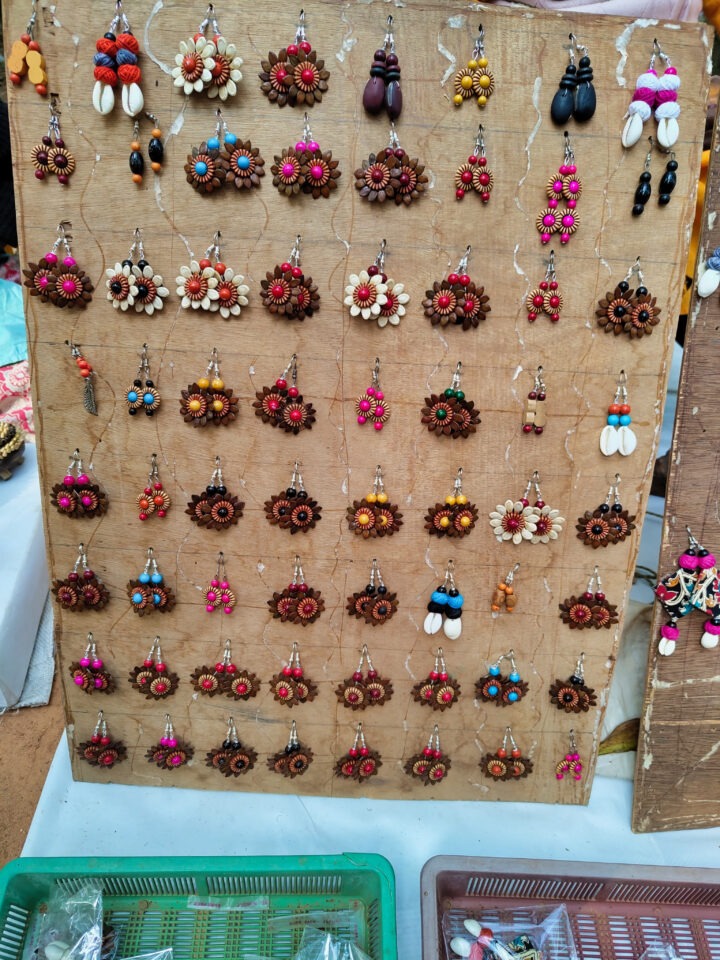 A display board showcases a variety of colorful earrings, including floral designs and bead accents, arranged in rows on a stand. Below, a green basket contains additional earring pairs.